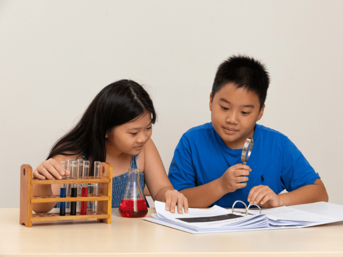 Girl looking at notes and boy holding a magnifying glass